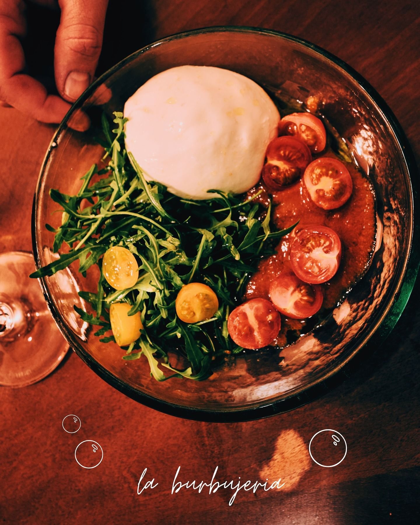 Ensalada con tomates, verduras y burrata, servida desde arriba, sobre una mesa de madera.
