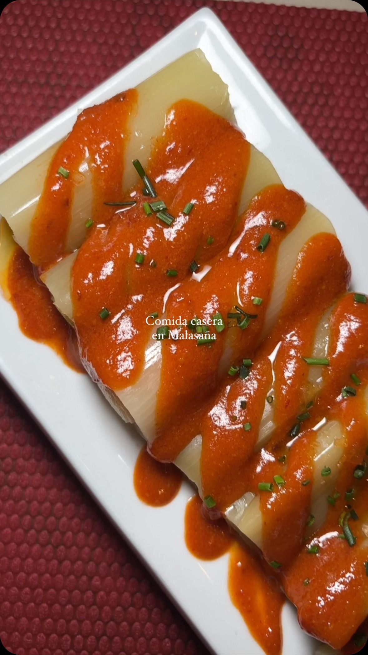 Postre blanco en rodajas cubierto con salsa roja de fresa en un plato cuadrado.