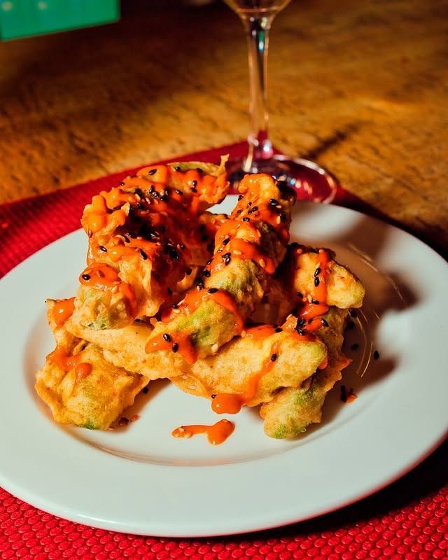 Aperitivo frito con salsa servido en un plato blanco con un mantel individual rojo y una copa de vino.