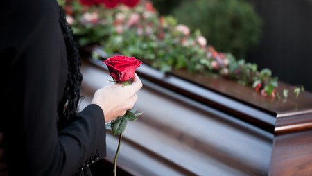 Femme tenant une rose rouge devant un cercueil