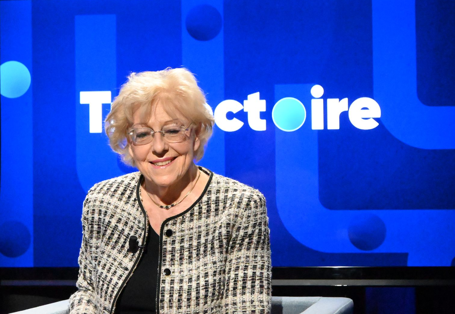 Femme en veste assise sur un plateau ; logo « Tractoire » sur fond bleu. Souriante.