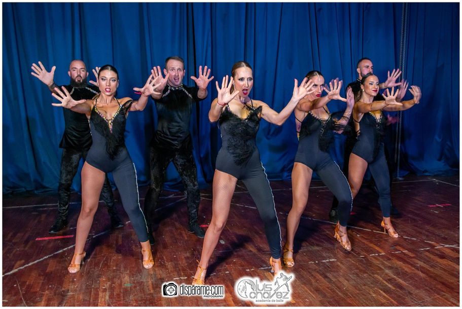 Un grupo de personas está bailando en un escenario frente a una cortina azul.