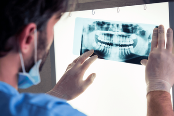 Dentista examinando una radiografía dental en una caja de luz, con las manos enguantadas en una clínica.