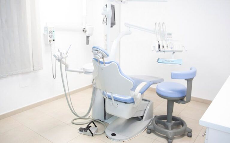 Sala de examen dental luminosa con silla, taburete y equipo aéreo en blanco y azul.