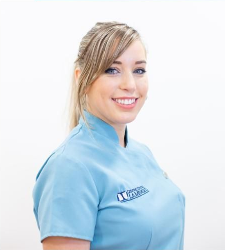 Mujer sonriente con uniforme azul claro sobre fondo blanco.