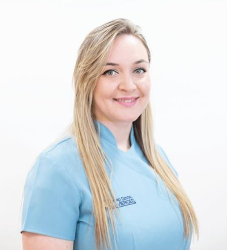 Retrato de una mujer sonriente con uniforme azul claro sobre fondo blanco.