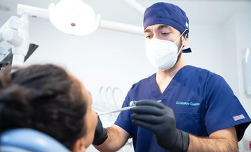 Un dentista con bata azul y mascarilla examina a un paciente durante un procedimiento dental.