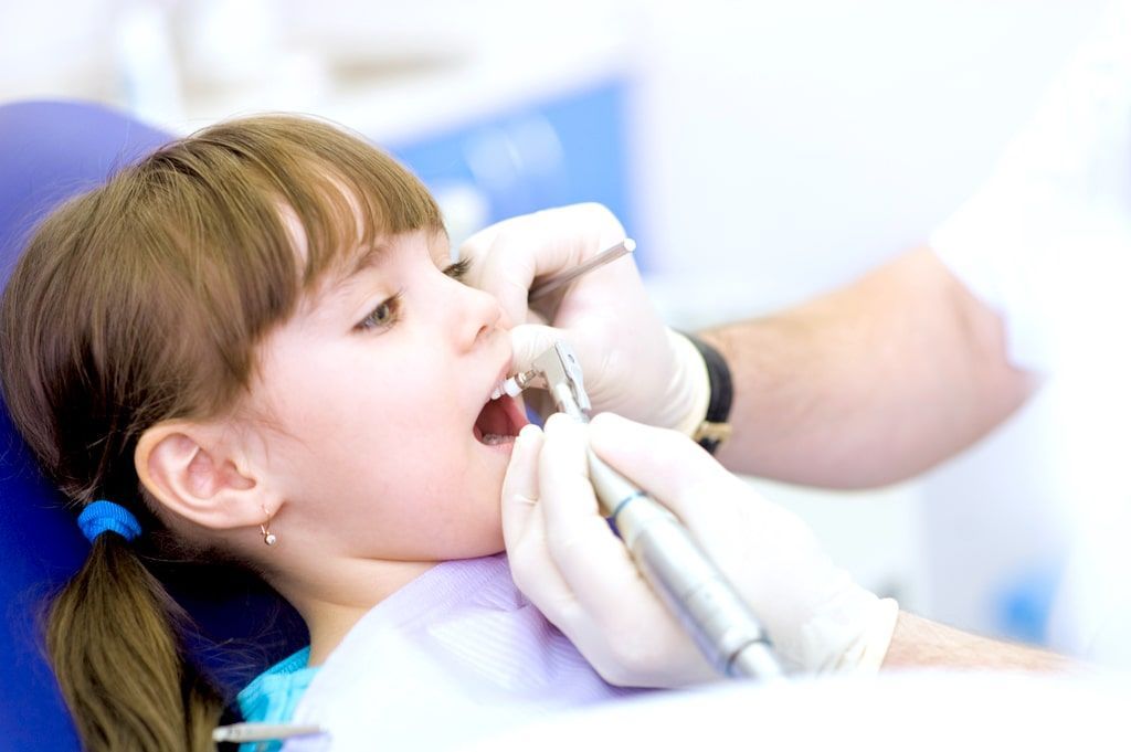 Un niño recibe tratamiento dental mientras un dentista con guantes utiliza un instrumento en una clínica bien iluminada.