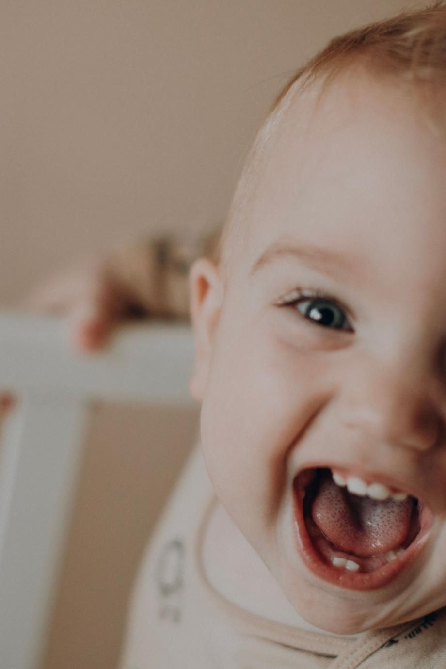 Niño pequeño sonriente con la boca abierta en un primer plano de un interior con iluminación tenue.