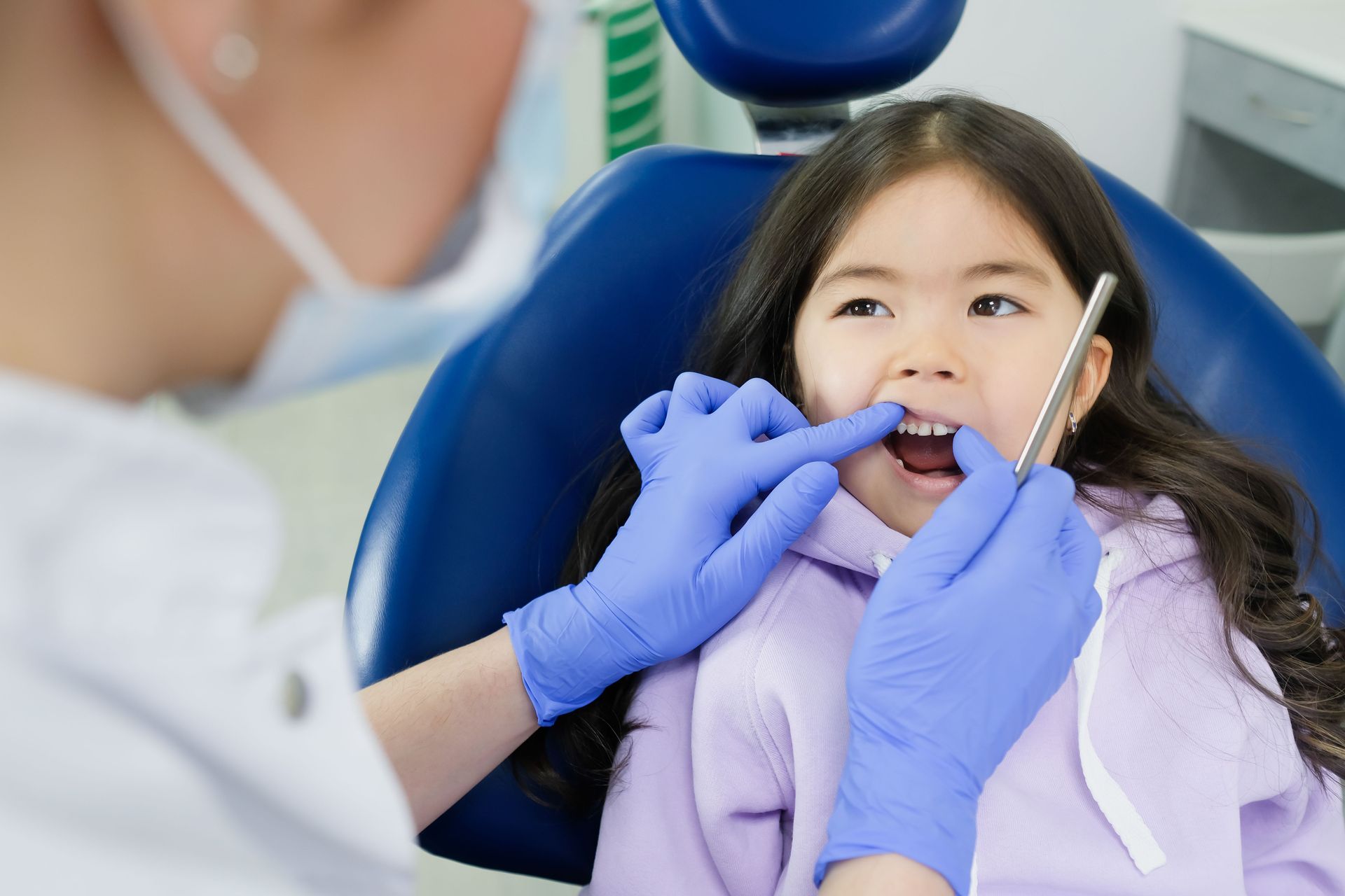 Un dentista examina la boca abierta de un niño con las manos enguantadas en un sillón dental.