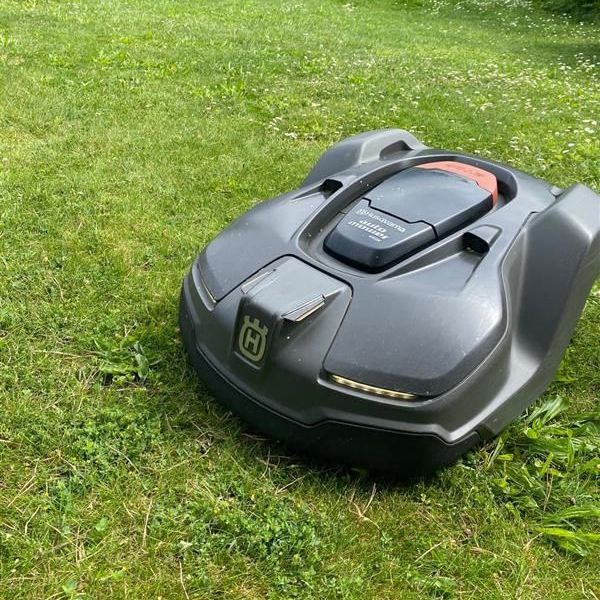 Une tondeuse à gazon robotisée verte et blanche est posée sur une pelouse verte luxuriante.