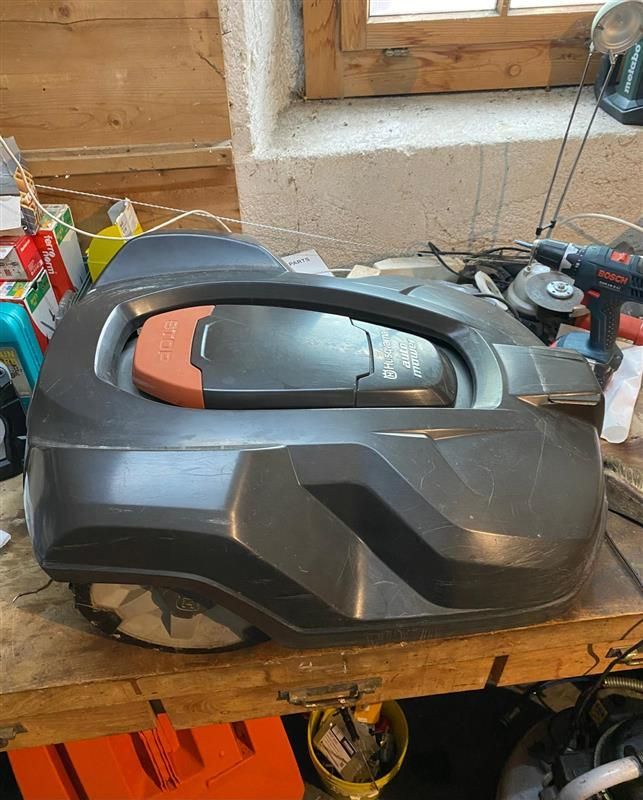 Une tondeuse à gazon robotisée est posée sur une table en bois.