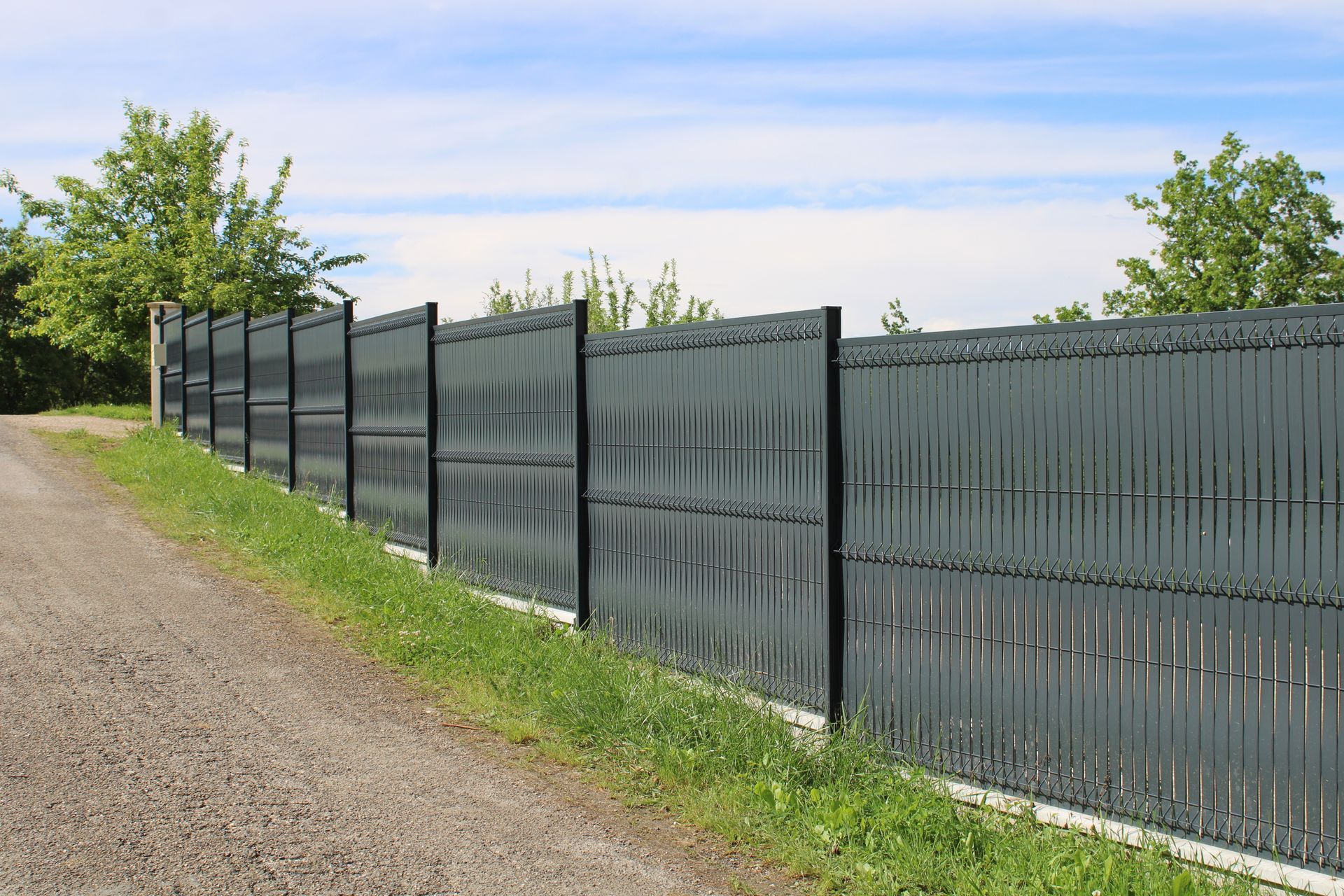 A black fence is along the side of a dirt road.