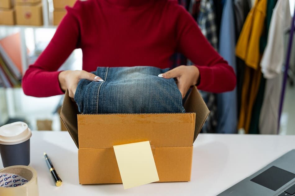 Una mujer está metiendo un par de jeans en una caja de cartón.