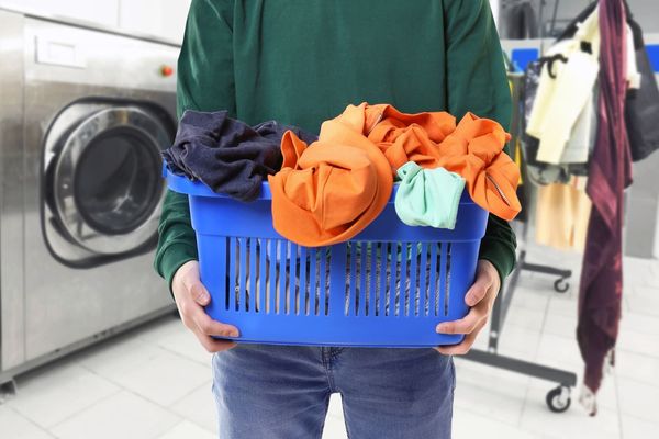 Una persona sostiene una cesta azul llena de ropa en una lavandería.