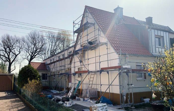 Haus im Umbau mit Gerüst und freiliegenden Außenwänden in einem sonnigen Garten