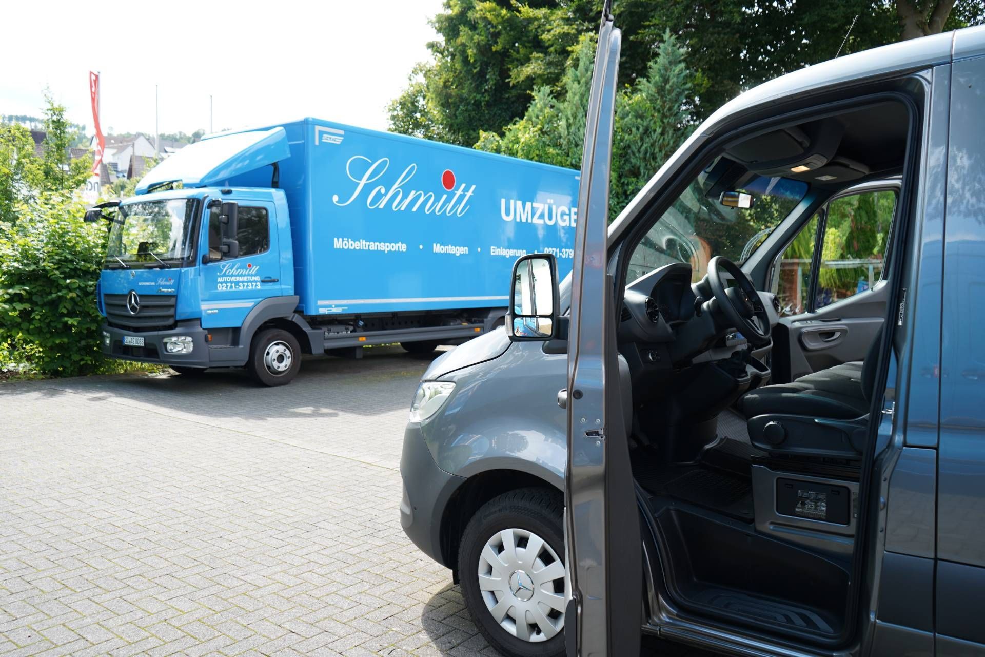 Ein blauer Schmidt-Truck steht neben einem grauen Lieferwagen