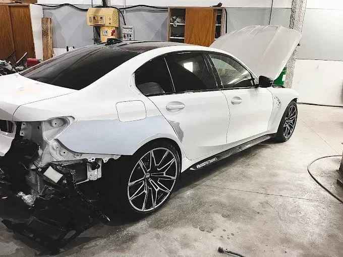 Un sedán BMW blanco con el parachoques trasero y las luces traseras desmontados en un garaje.