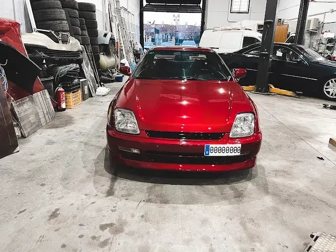 Un Honda Prelude de quinta generación de color rojo brillante estacionado dentro de un taller mecánico muy iluminado.