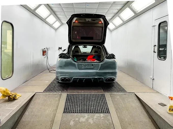 Un coche gris con el maletero abierto aparcado dentro de una cabina de pintura profesional para carrocerías.