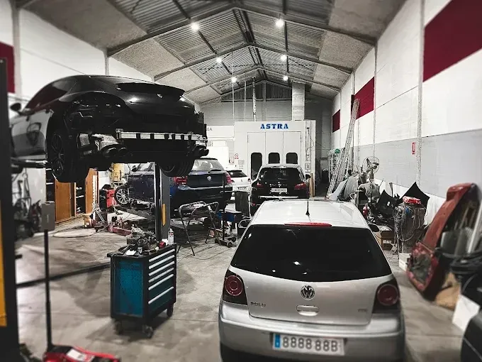 Un taller de reparación de automóviles con un coche negro en un elevador y un coche plateado aparcado en el suelo.