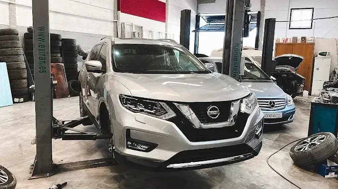 Un SUV Nissan plateado elevado en un elevador de coches en un taller.