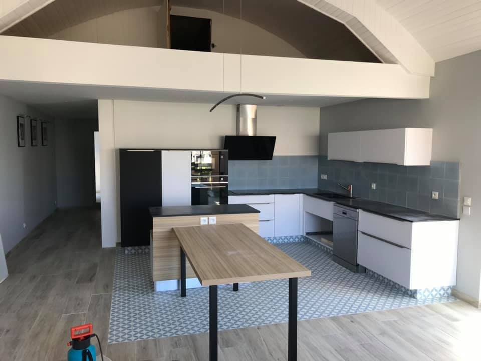 Rénovation d'une cuisine avec mobilier planc, revêtement mural bleu-gris, et table centrale noir-bois