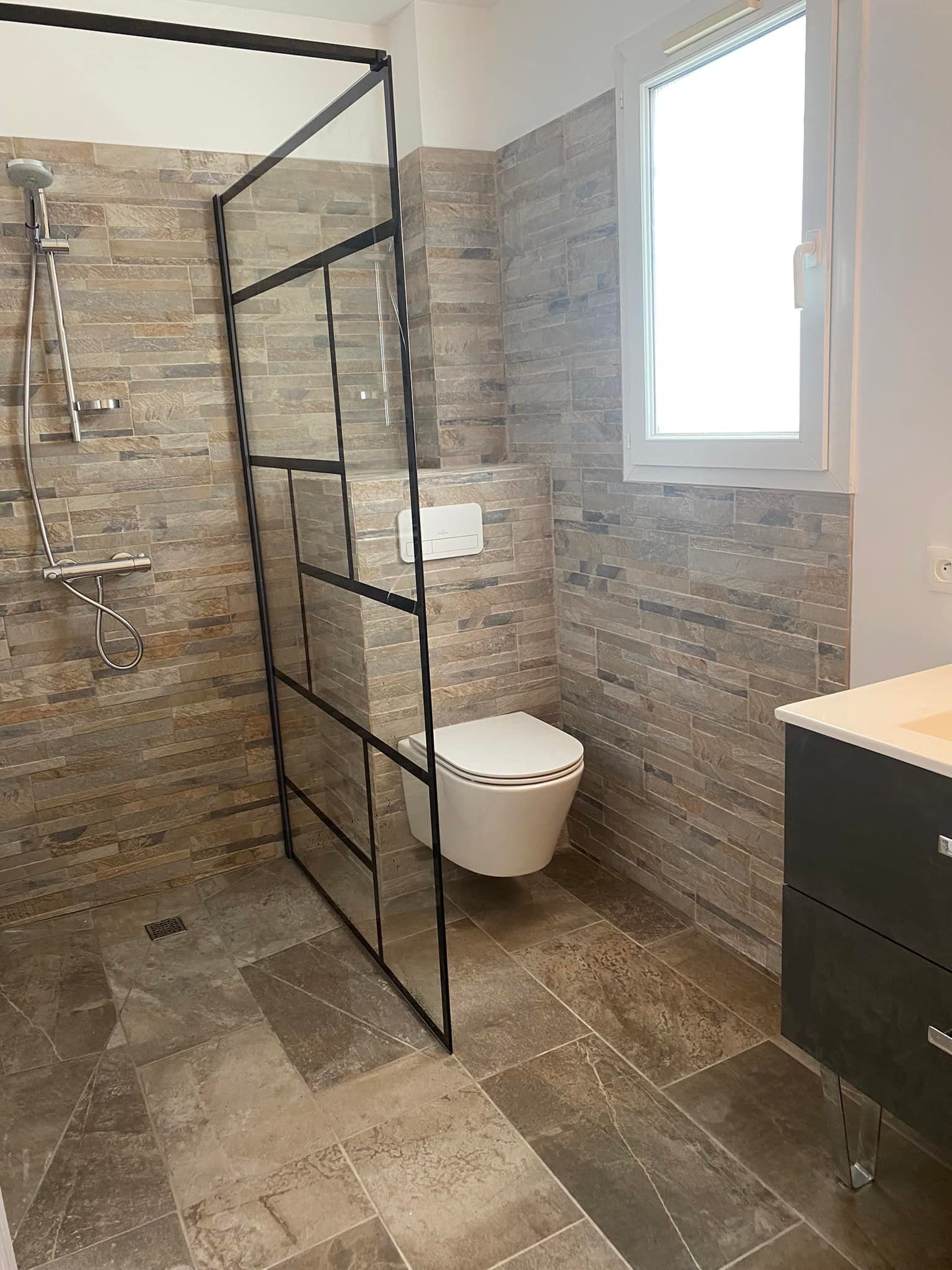 Espace toilettes aménagé en salle de bains séparé d'une cabine de douche par une paroi vitrée