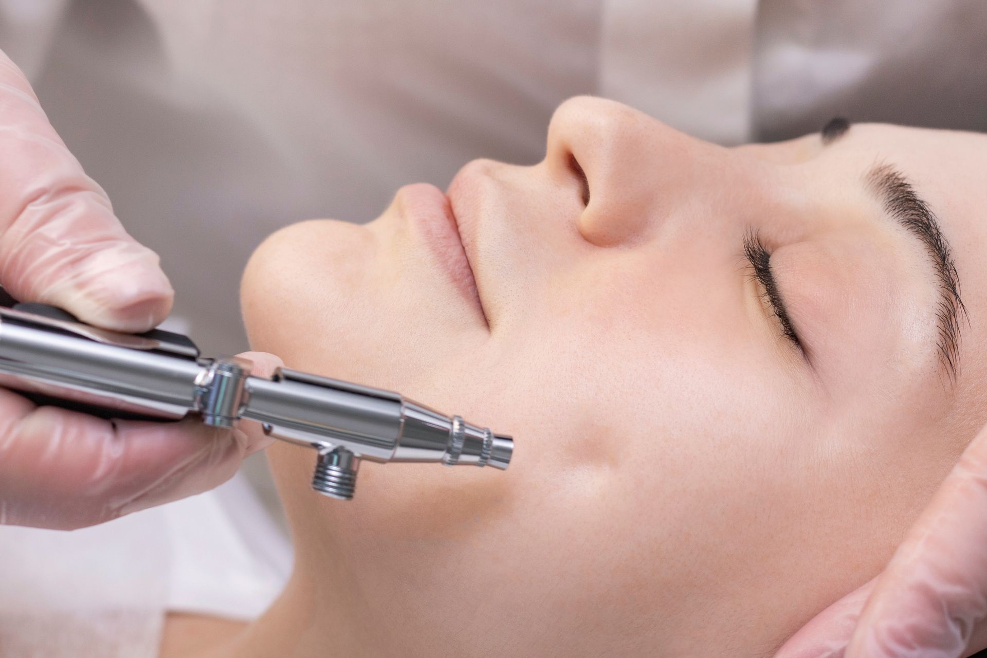 Mains gantées utilisant un appareil de soin du visage sur le visage d'une femme lors d'un soin en spa