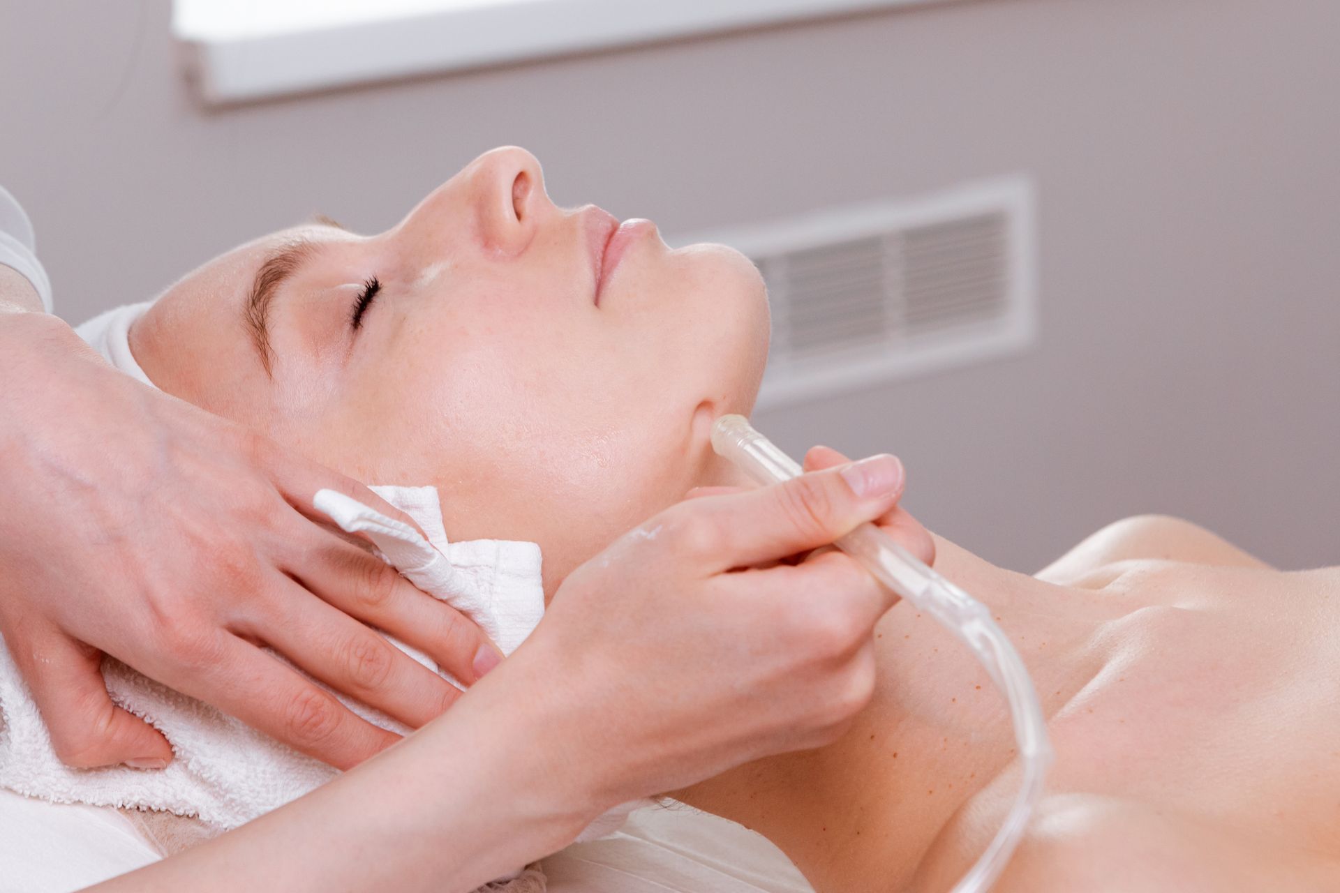 Une femme reçoit un soin du visage avec application de crème sur le cou et le visage dans un spa.