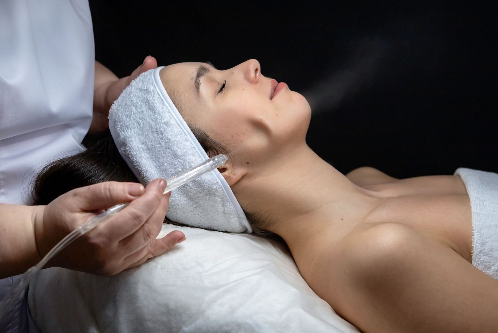 Soin spa : une femme est allongée sur une table pendant qu'un praticien applique un sérum facial à l'aide d'un compte-gouttes.