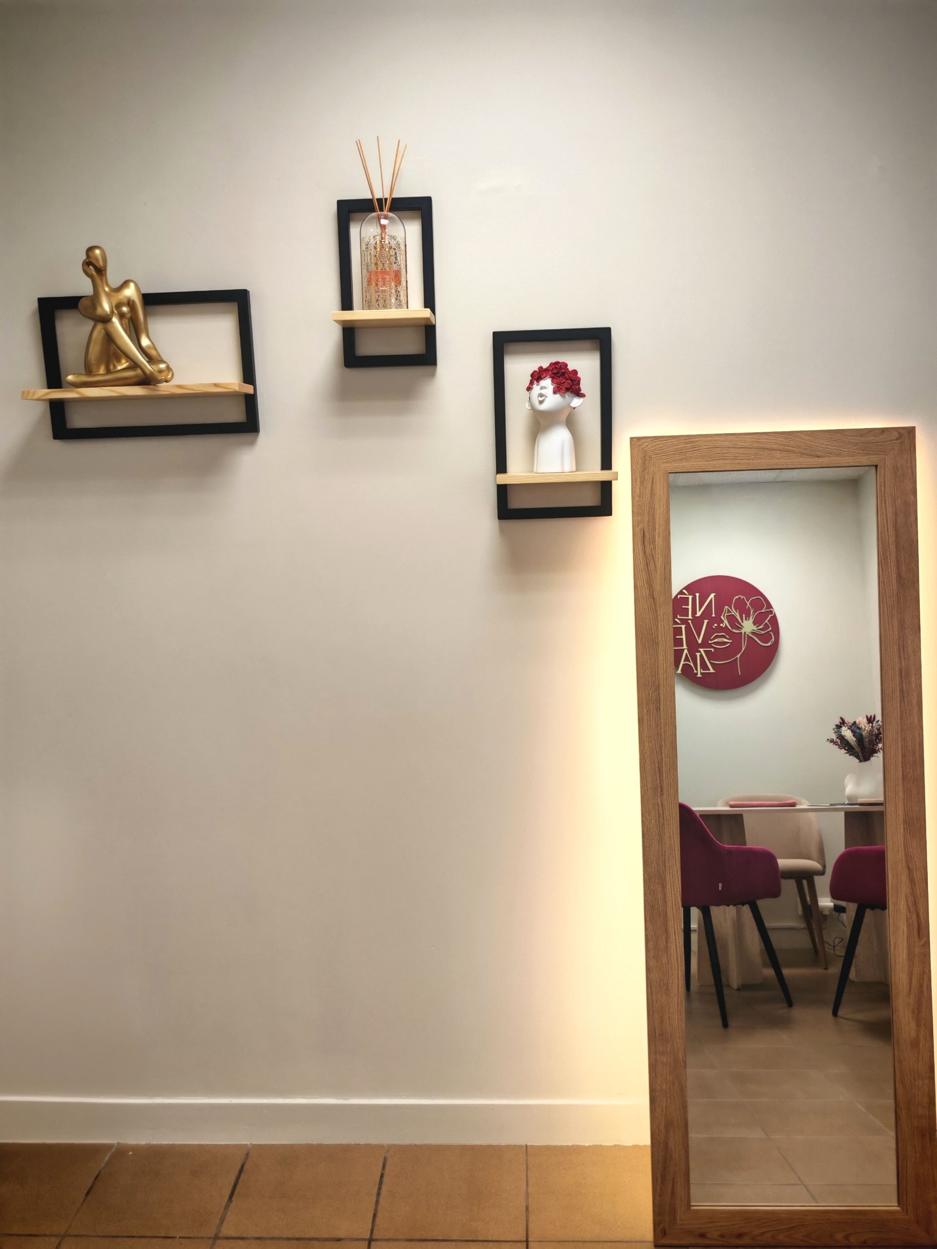 Un petit mur façon galerie avec des étagères et des œuvres d'art, ainsi qu'un miroir à cadre en bois reflétant une décoration rouge et des chaises.