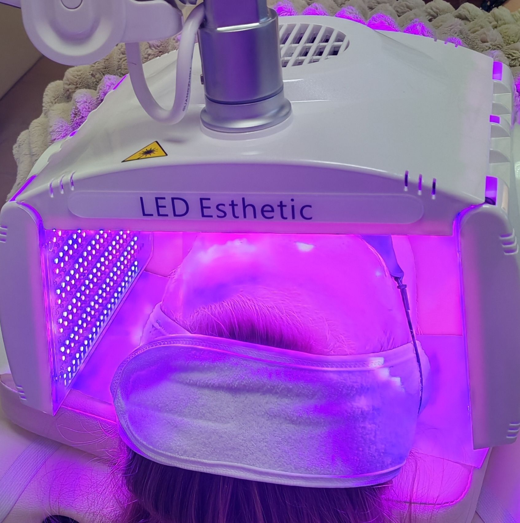 Personne sous une capuche de luminothérapie esthétique à LED violettes avec un masque facial