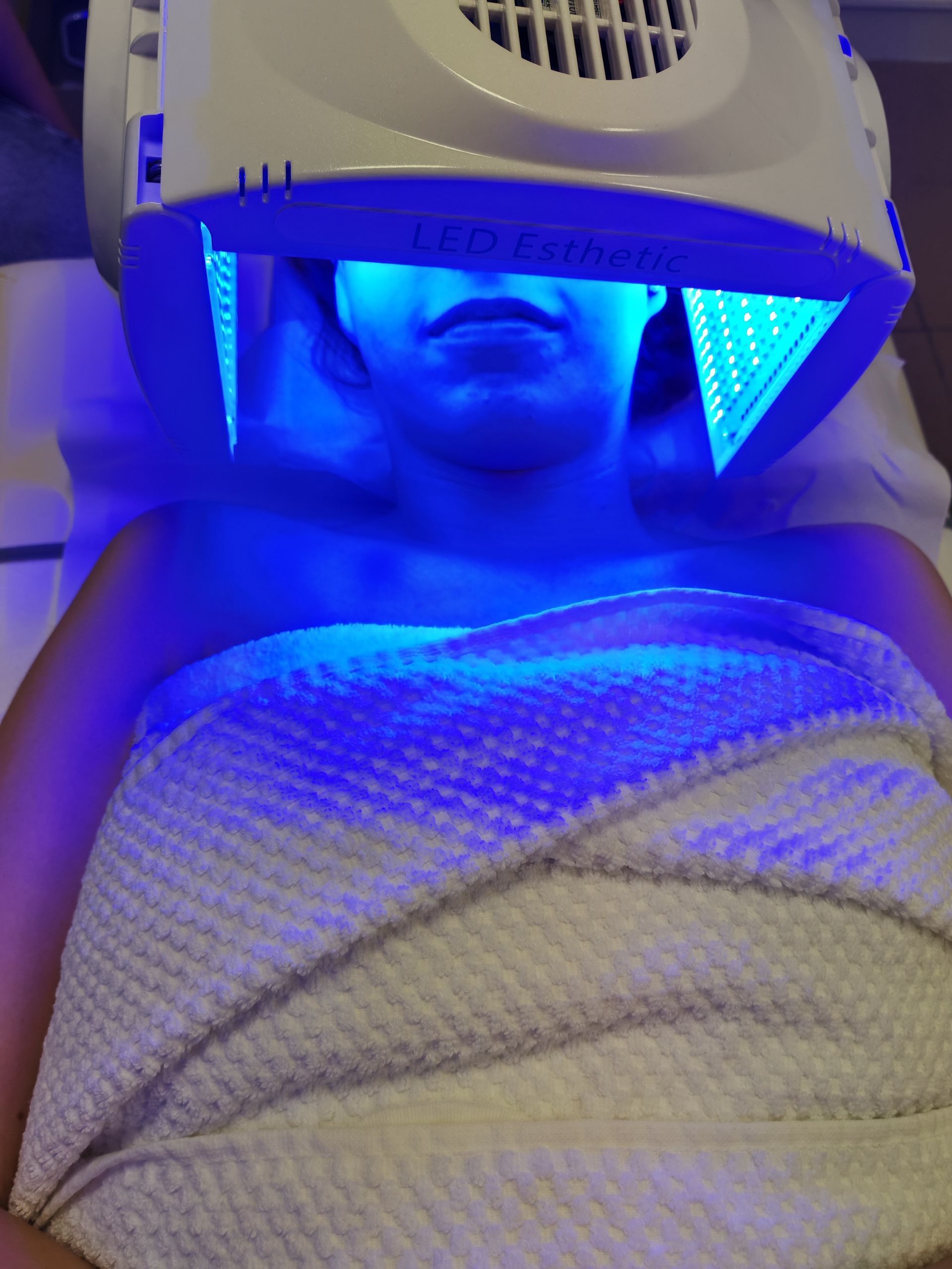 Personne sous un masque de soin du visage à lumière bleue, enveloppée dans une couverture blanche.