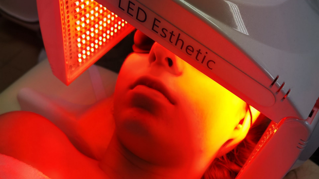 Personne recevant un soin du visage aux LED rouges sous un appareil lumineux