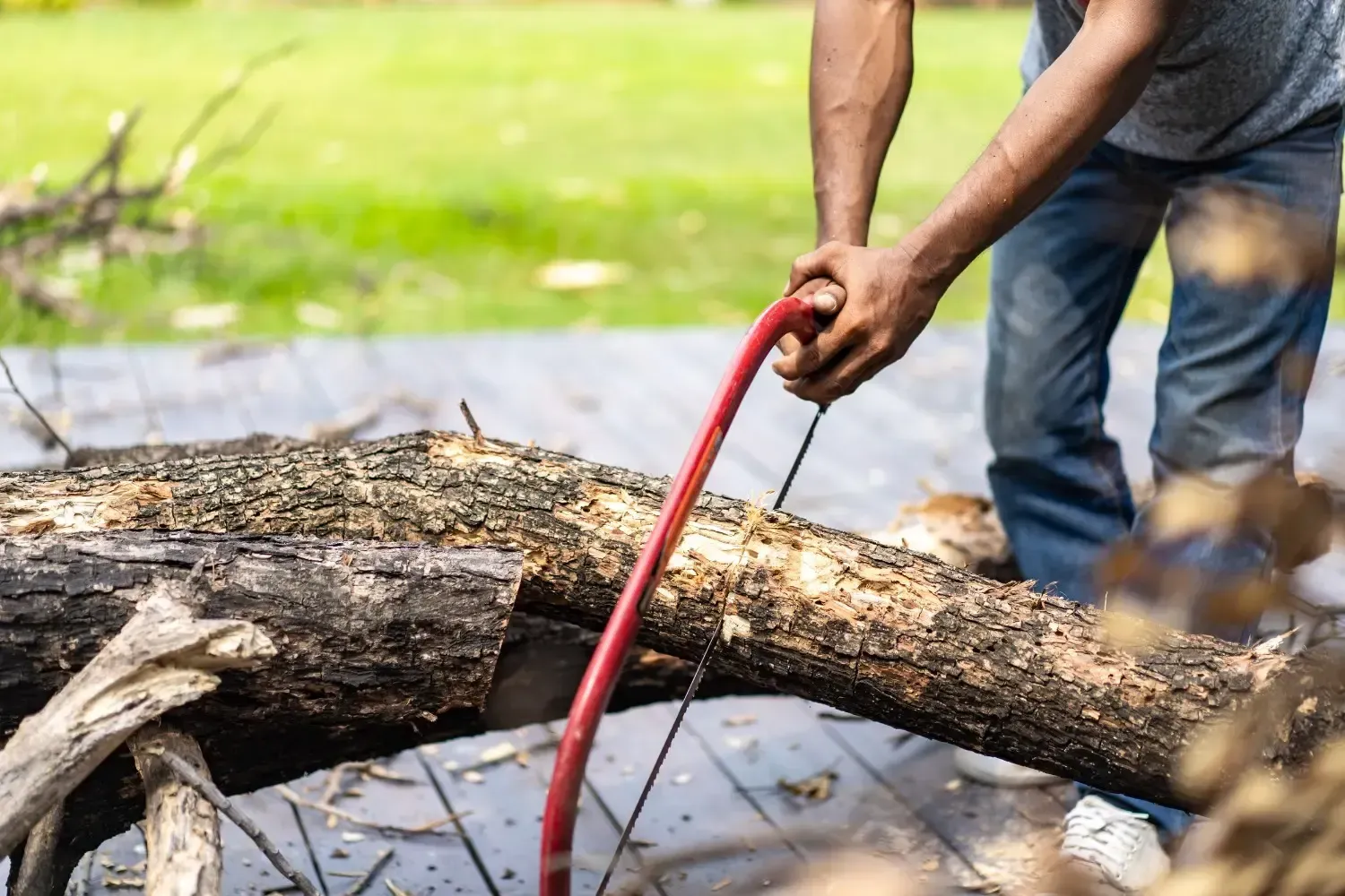 Persona cortando un tronco al aire libre con una sierra de mano roja.