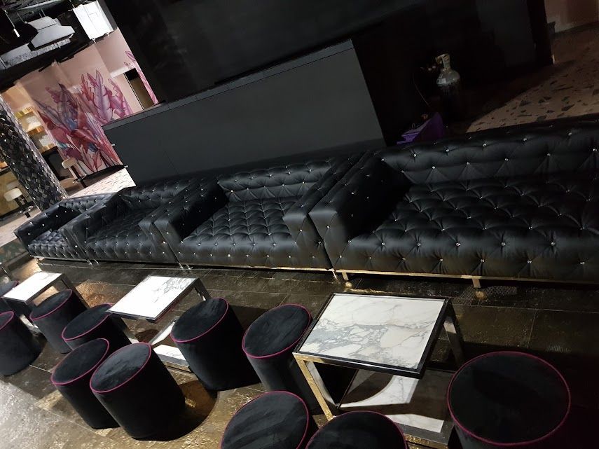 Interior de una tienda con botas sobre mesas. El local tiene techos altos, un mural y asientos.