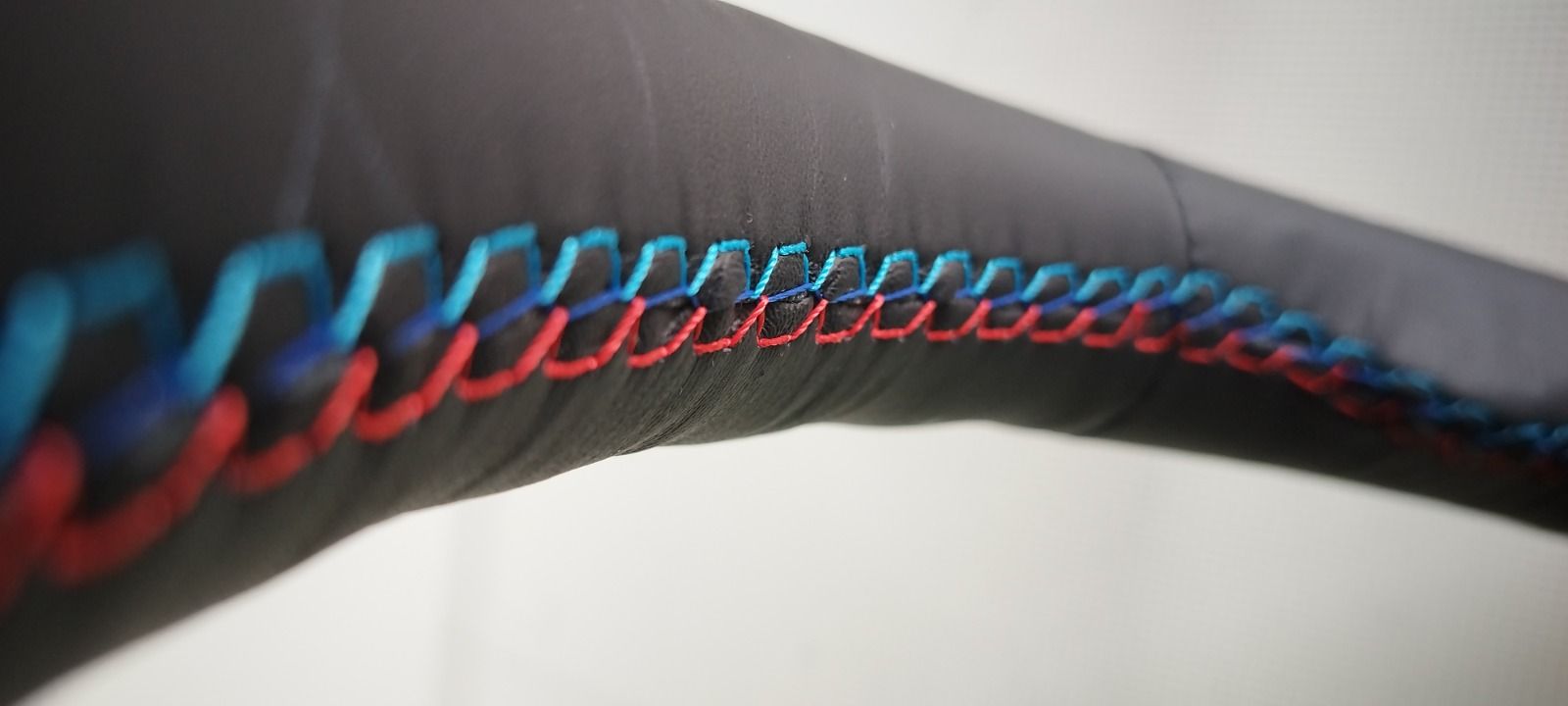 Primer plano de tela negra con costuras azules y rojas, posiblemente detalle del interior de un automóvil.