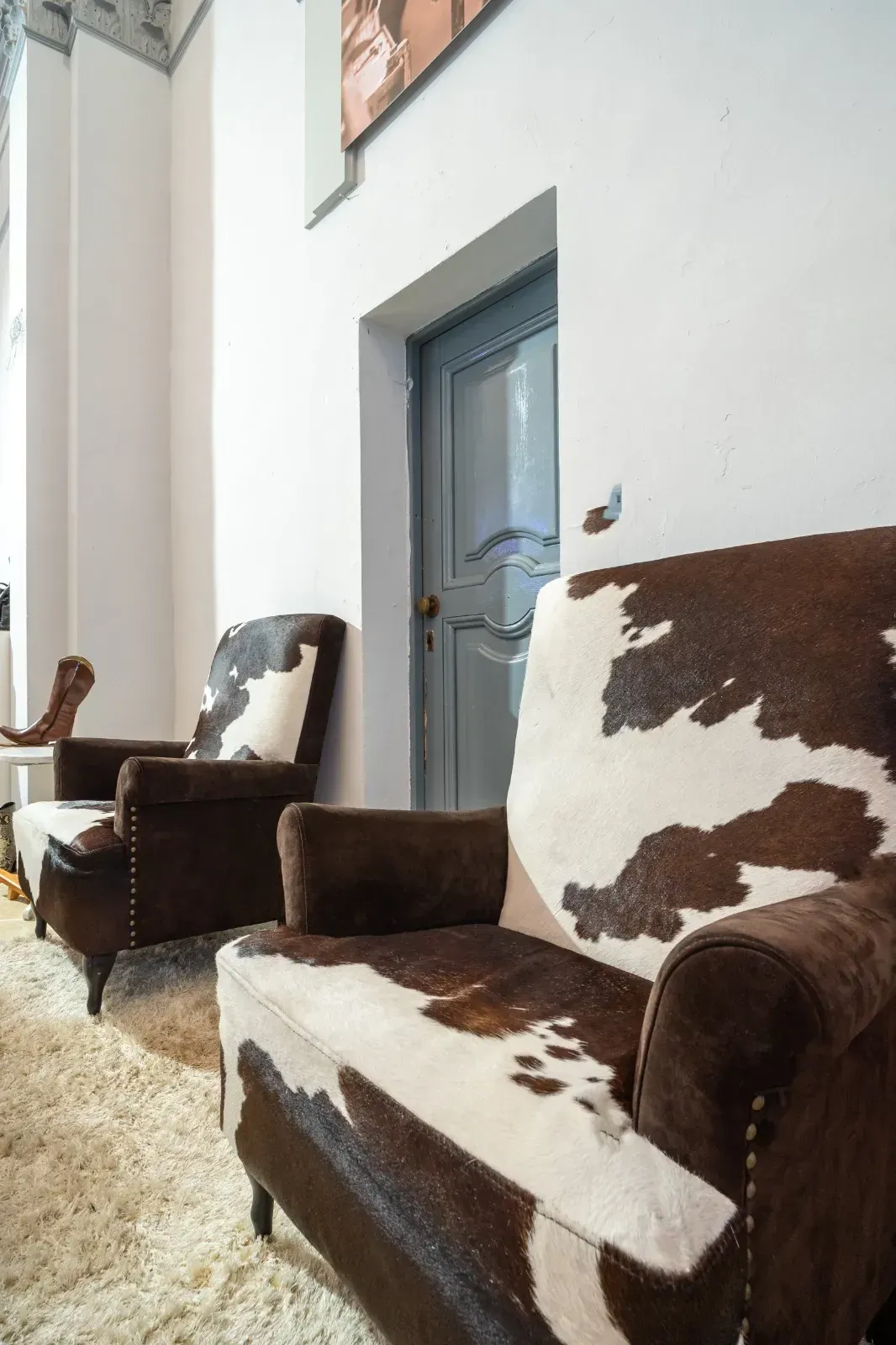 Dos sillones de piel de vaca de color marrón y blanco delante de una puerta azul y una pared blanca.
