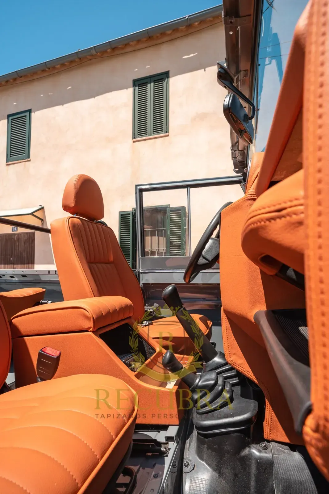 Interior de cuero naranja de un automóvil, con atención a los asientos y la consola, con un edificio al fondo.