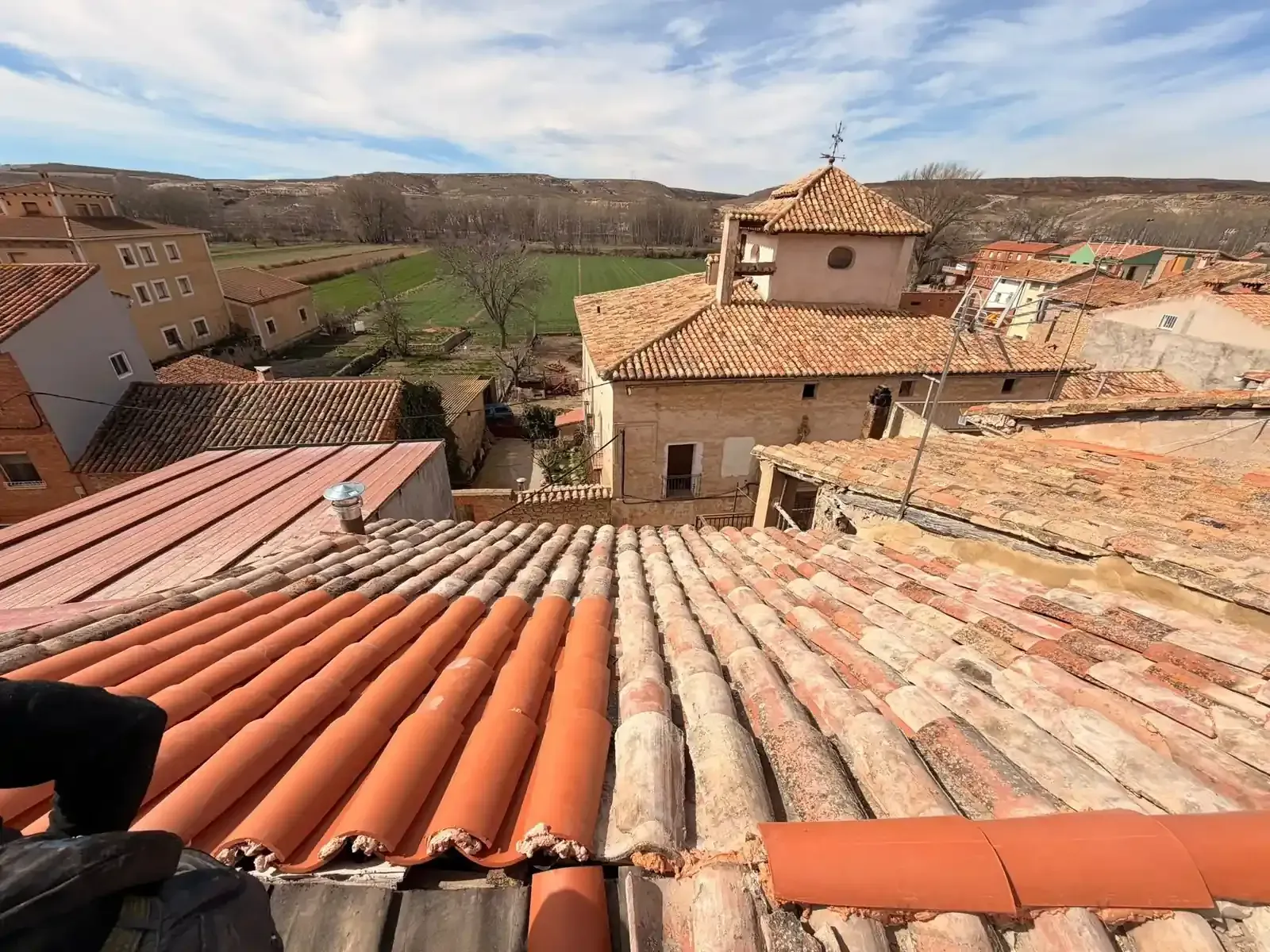 Vista desde un tejado con tejas de terracota, con vistas a un pueblo español con una iglesia y los campos que lo rodean.