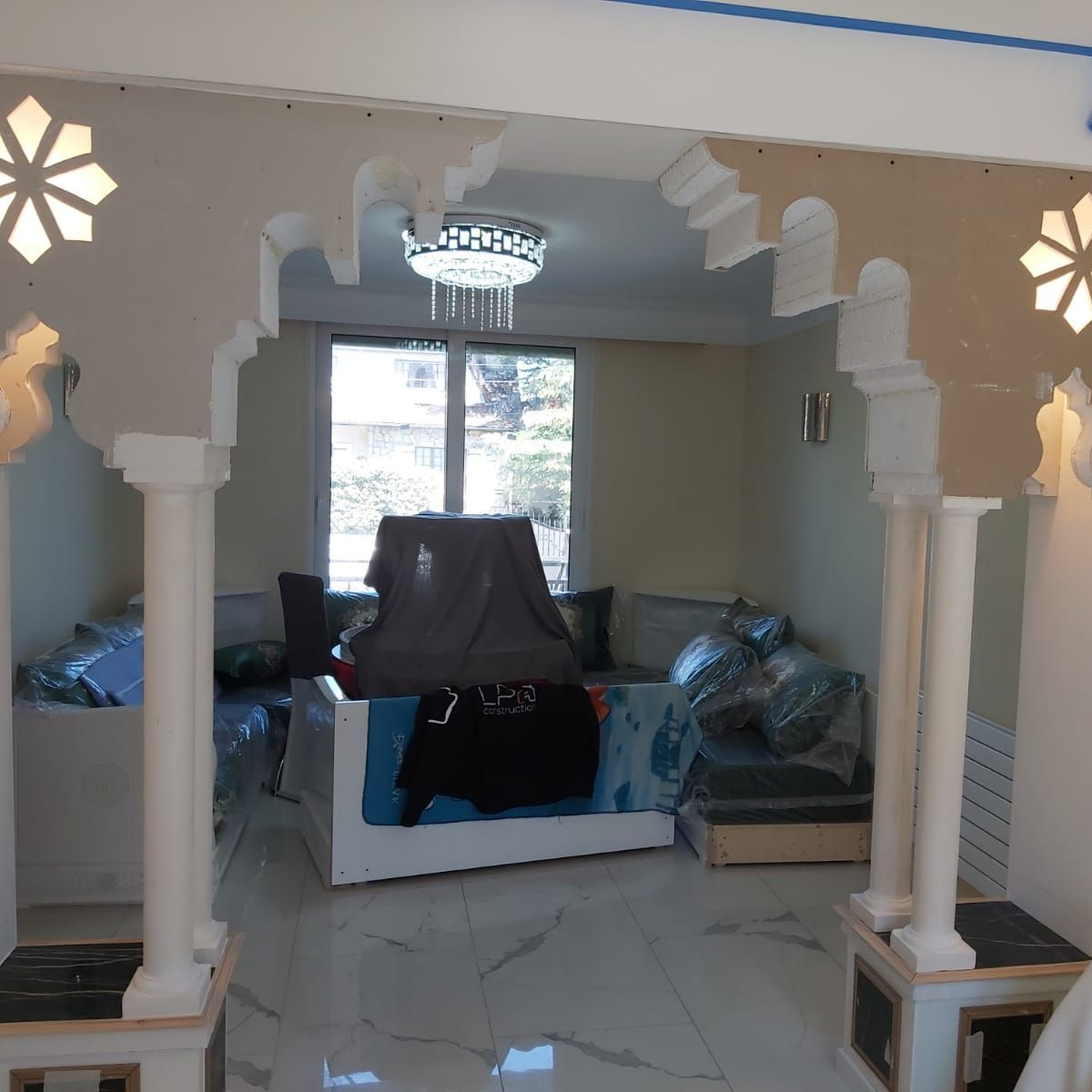 Intérieur du salon avec arche ornée, banquette intégrée, grandes fenêtres et lustre.