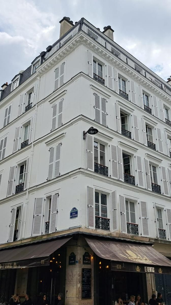 Immeuble blanc avec volets au-dessus d'un restaurant. Un immeuble d'angle à Paris.