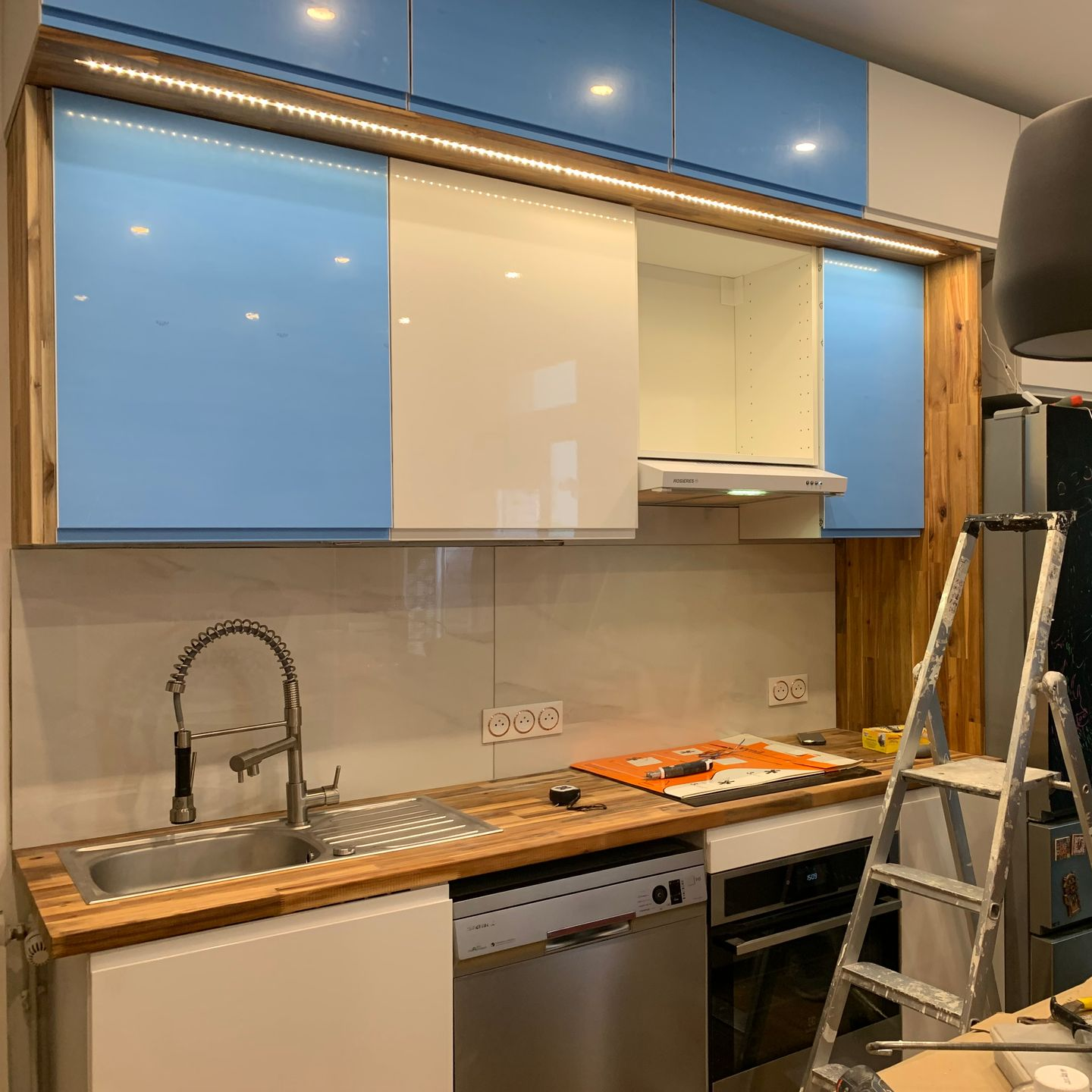 Cuisine équipée : meubles bleus et blancs, touches de bois et électroménager en inox. Évier et four visibles.