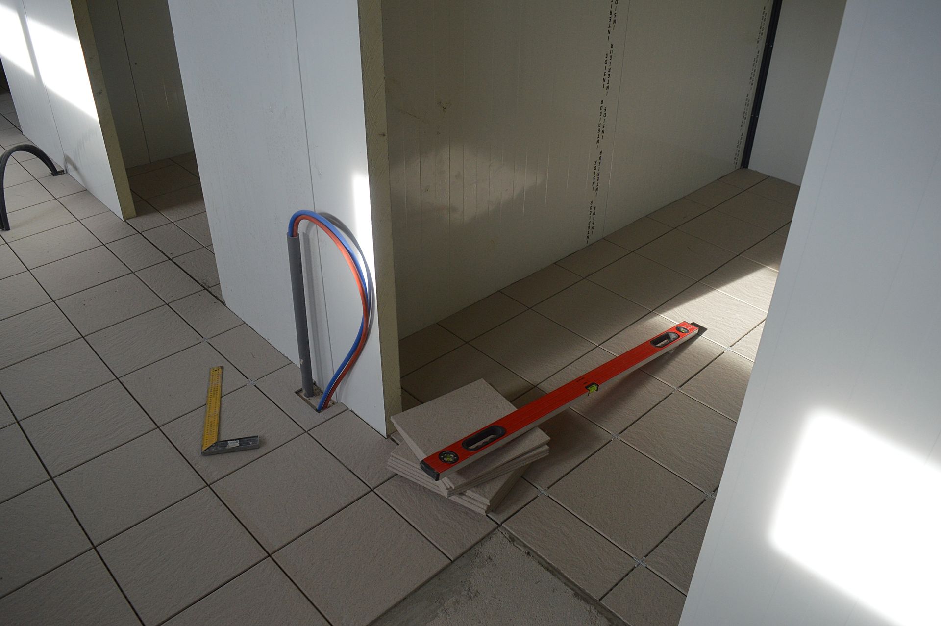 Intérieur d'un chantier de construction avec sol carrelé. Outils et matériaux de nivellement au sol près d'un mur dont l'isolation est apparente.