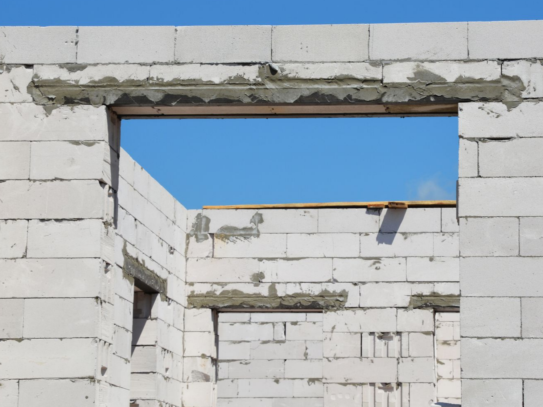 Mur en construction avec ouverture pour fenêtre, en parpaings blancs, ciel bleu.