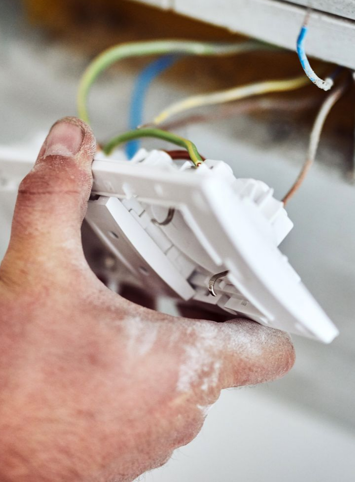 Installation manuelle d'une prise électrique blanche. Les fils sont visibles : bleu, marron, vert/jaune et blanc.