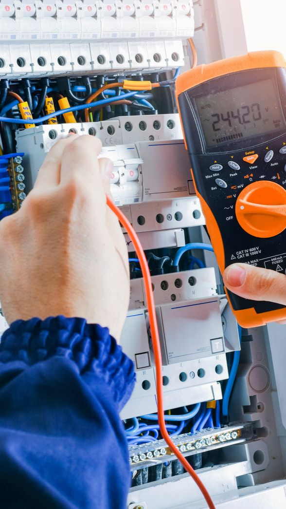 Un électricien utilise un multimètre pour tester un circuit dans un tableau électrique.