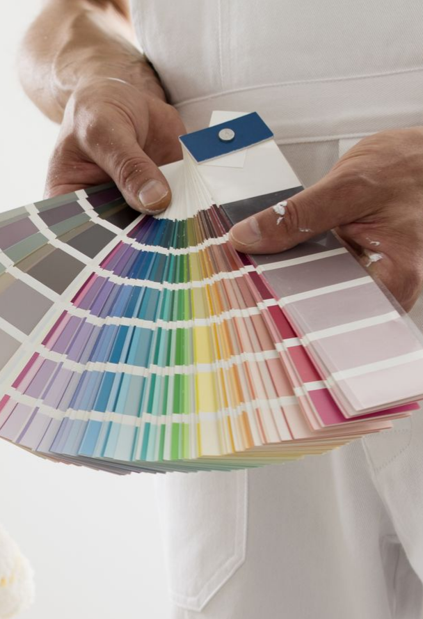 Une personne portant un tablier blanc, tenant un éventail d'échantillons de peinture, choisit une teinte.