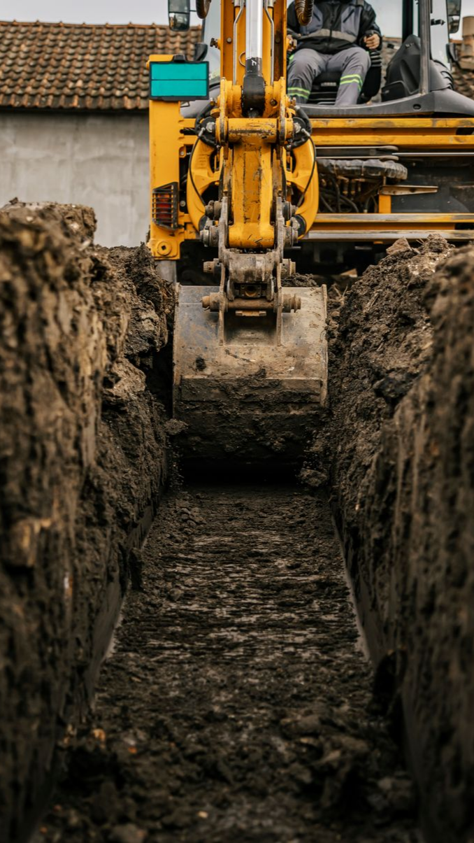 Une pelleteuse jaune creuse une longue et étroite tranchée dans un sol boueux.